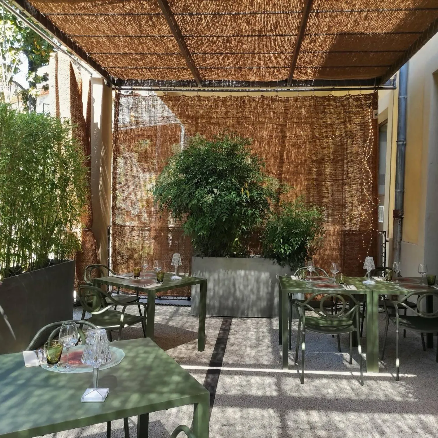 Terrasse ombragée sous une pergola en fibres naturelles, tables vert olive