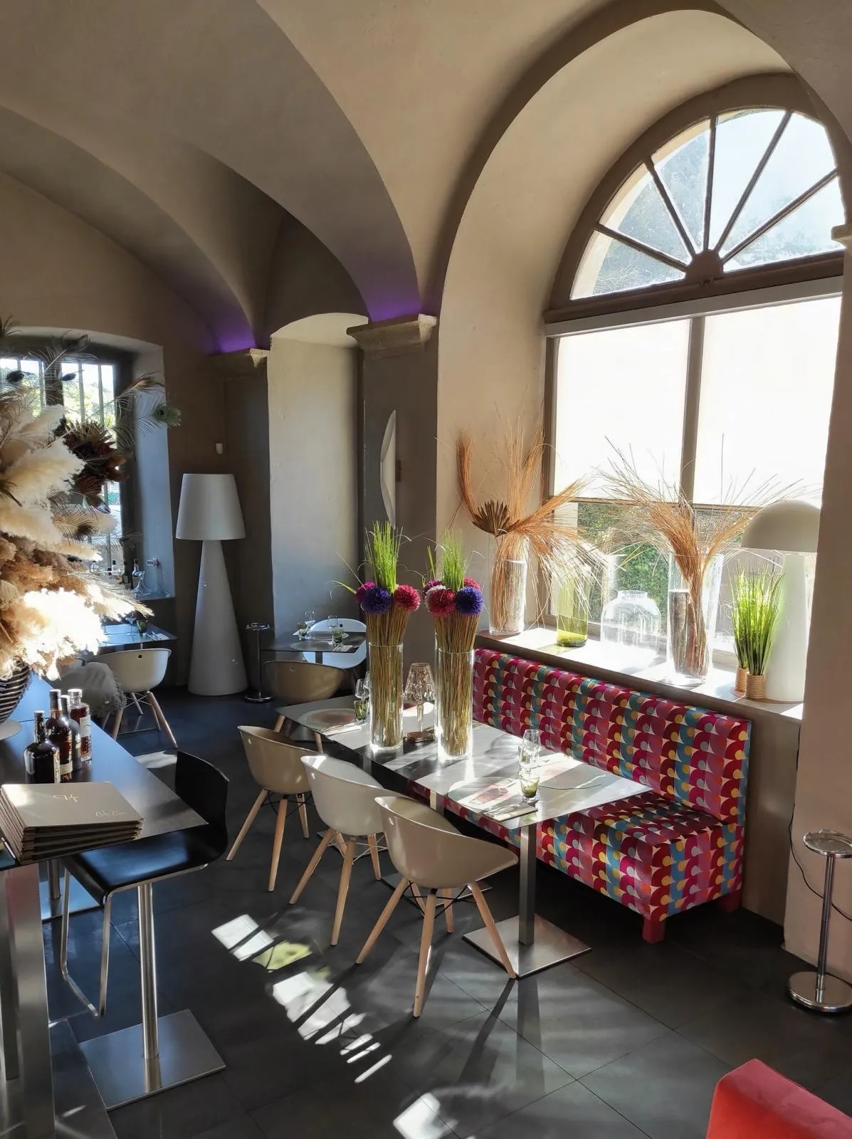 Salle voûtée en pierre, banquette en velours à motifs et grande fenêtre en arc