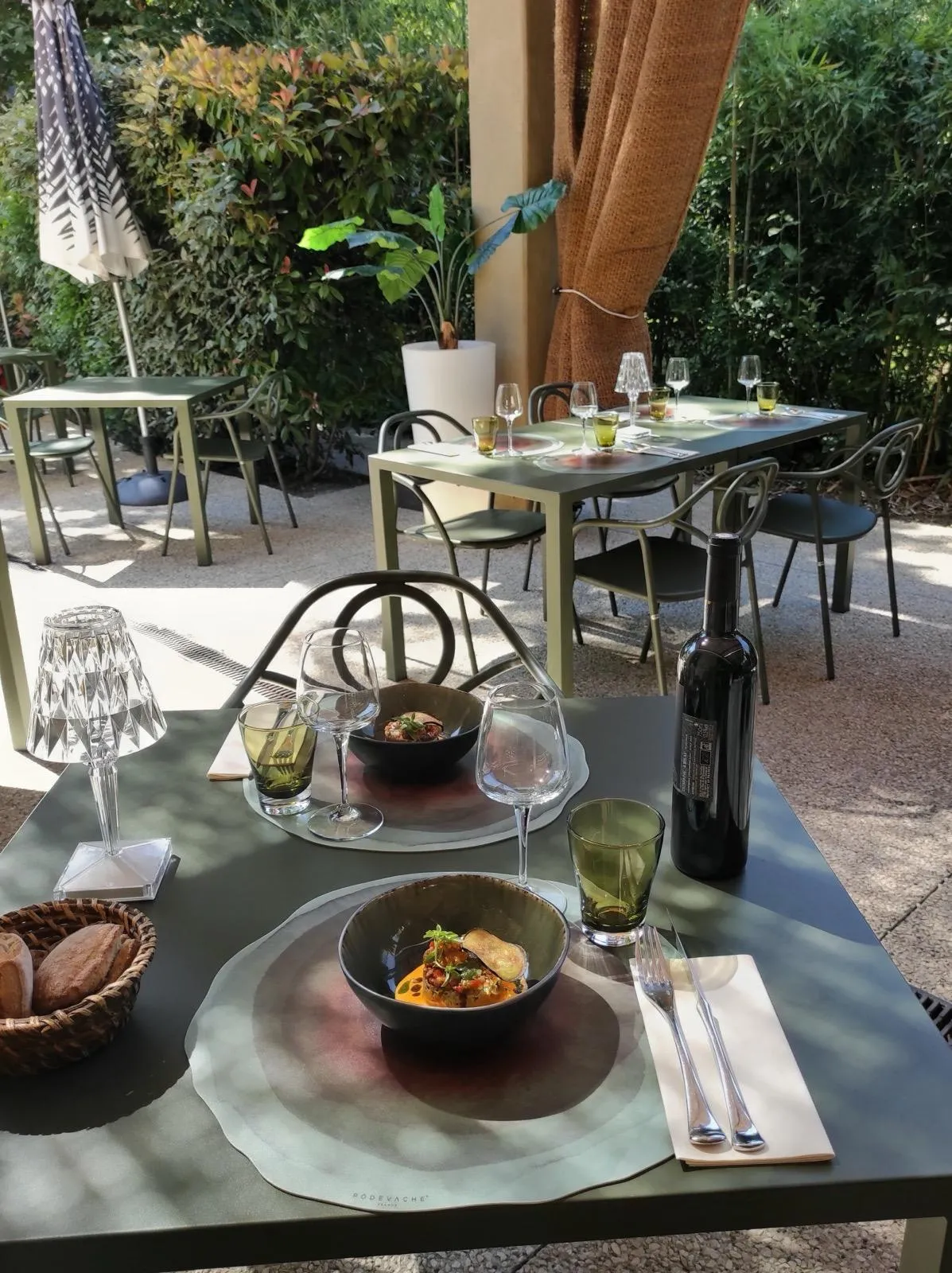 Table dressée en terrasse avec deux assiettes, vin rouge et pain